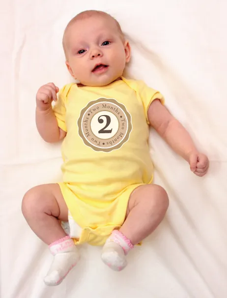 Baby in a yellow onesie with a 2-month sticker.
